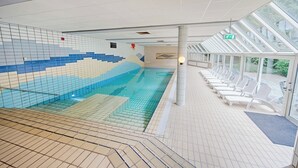 An indoor swimming pool with a tiled mural, sun loungers, and a glass-enclosed area with a view. - Peaceful Getaway — Free Parking, Indoor Pool, and Everything You Need to Unwind (Lochem)