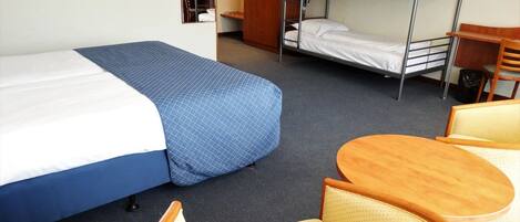 Una habitación de hotel con literas, una cama individual, una silla de madera, una pequeña mesa redonda y un armario.