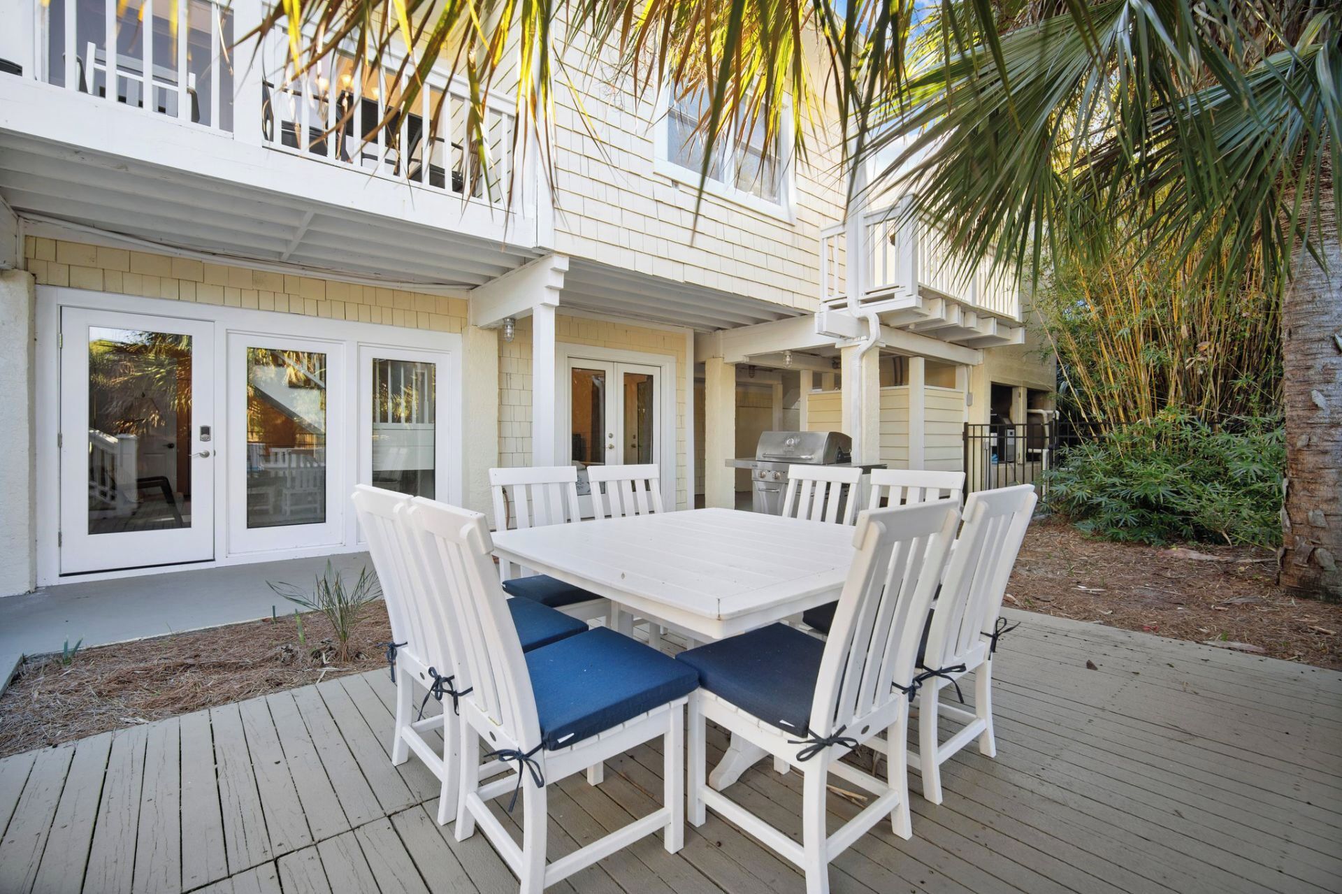 A covered patio with a white table and chairs, a grill, and a view of the house.