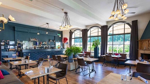 Een restaurant met houten tafels en stoelen, een bar en grote ramen met uitzicht op het buitengebied.