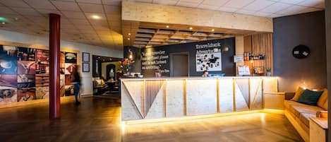 A reception area with a wooden counter, a seating area, and a wall with travel-related posters.
