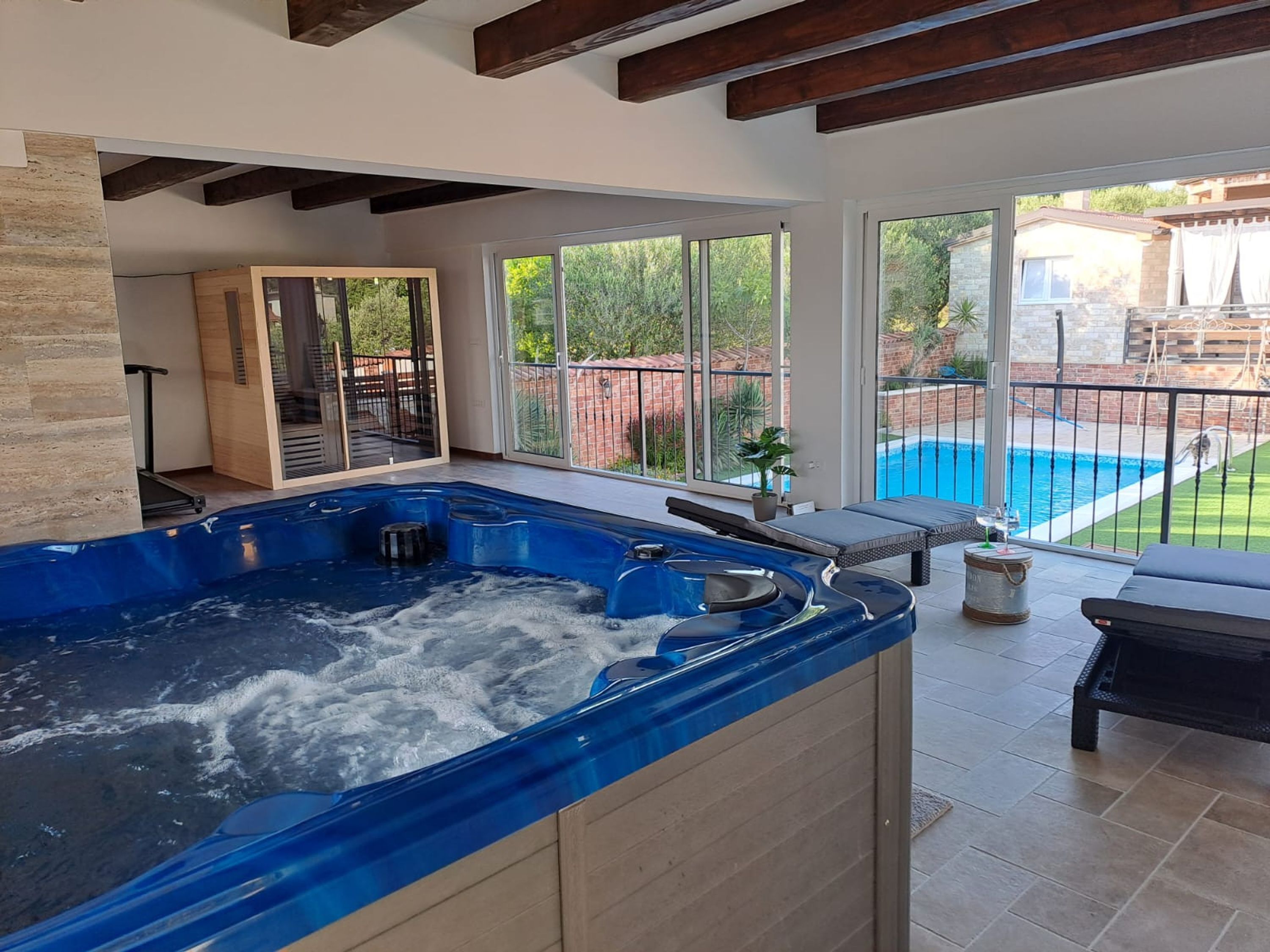 A modern indoor swimming pool with a hot tub, large windows, and a view of an outdoor pool.