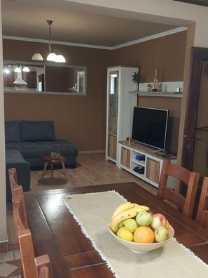 A living room with a sofa, a dining table with a fruit bowl, a TV on a stand, and a cabinet. - Villa Nicoletta in Polaca (Polaca)