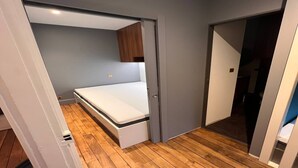 Ein kleines Schlafzimmer mit einem Einzelbett, Holzboden und grauer Wand.