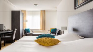 A hotel room with two beds, a desk, a chair, and a window with curtains.