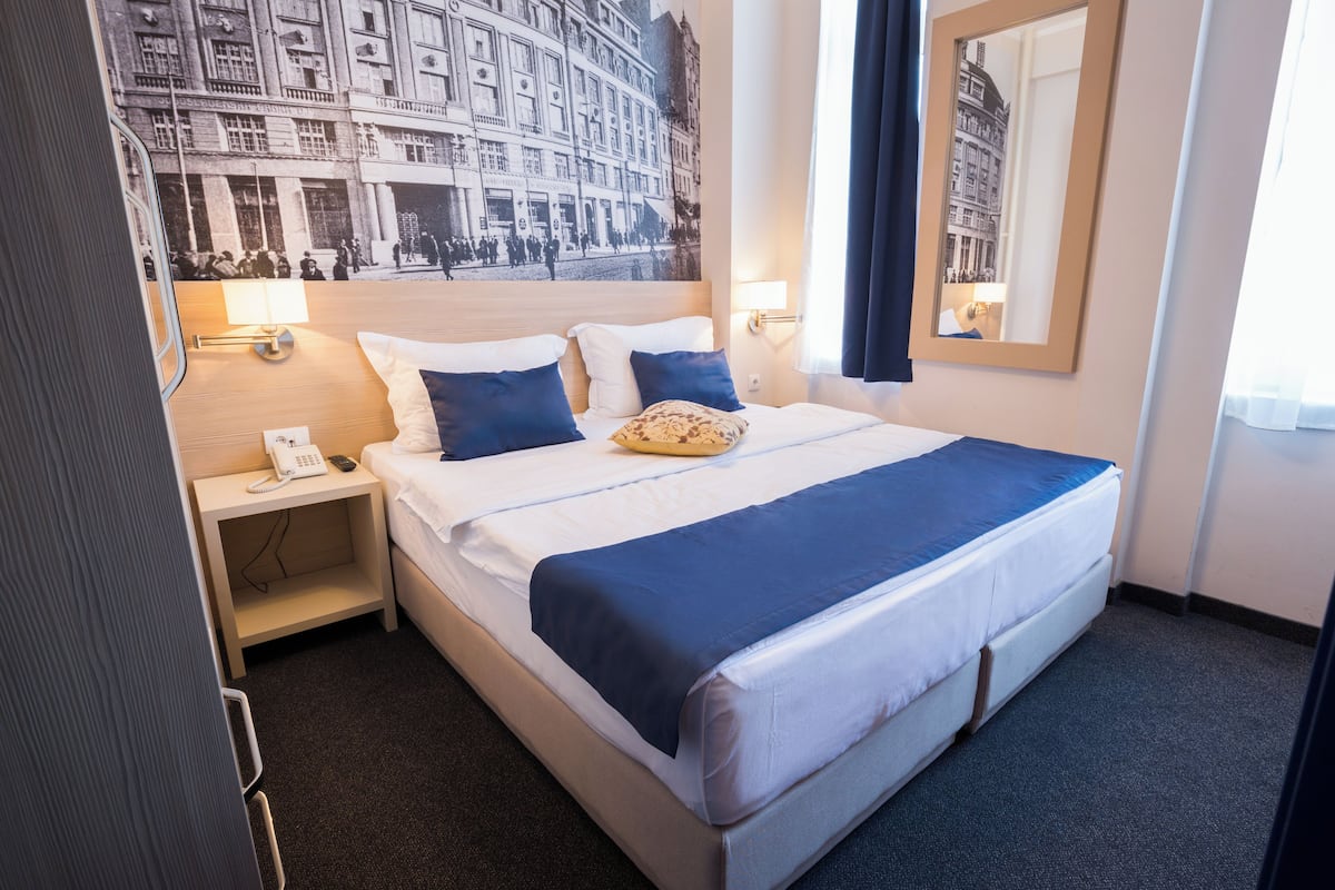 A hotel room with a bed, a nightstand with a lamp, a phone, and a wall-mounted mirror.