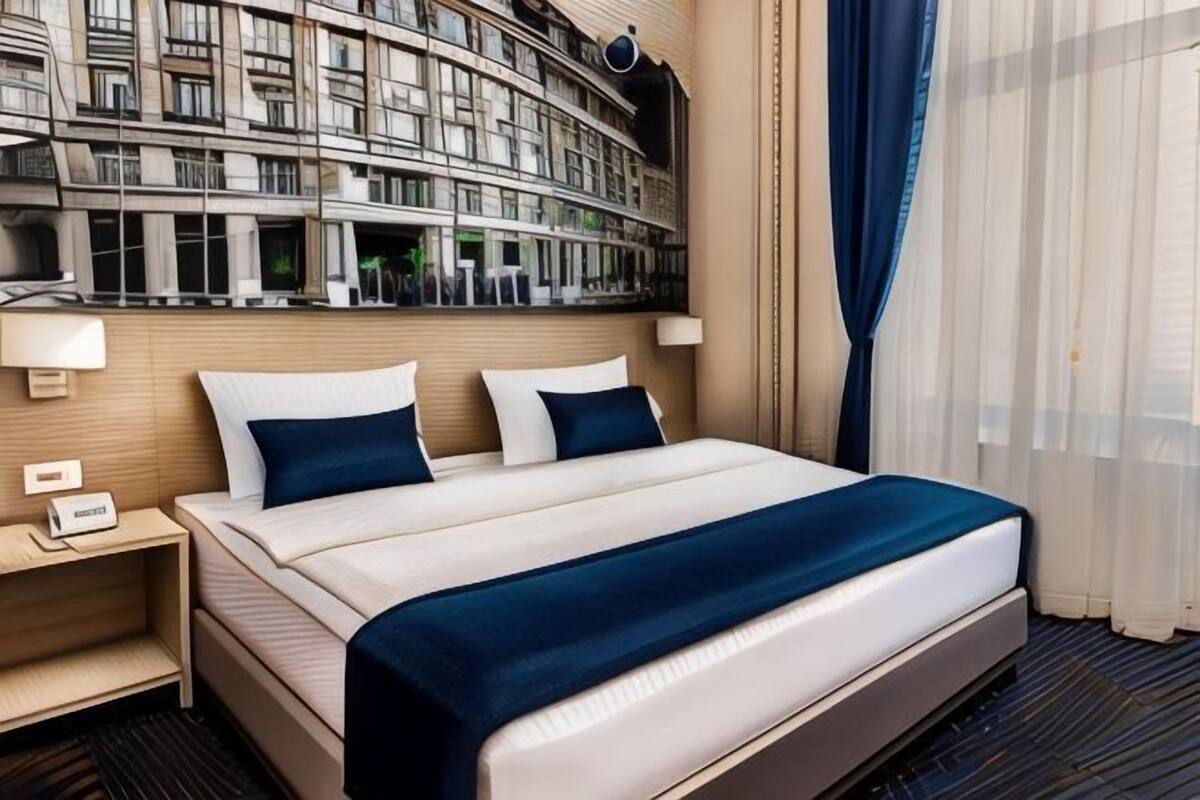 A hotel room with a large bed, a nightstand, a mirror, and a view of a building.