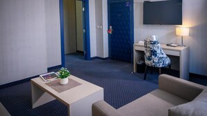 A hotel room with a bed, a desk, a chair, a TV, and a small table with a plant and a magazine. - Five Points Square - City Center (Belgrade)