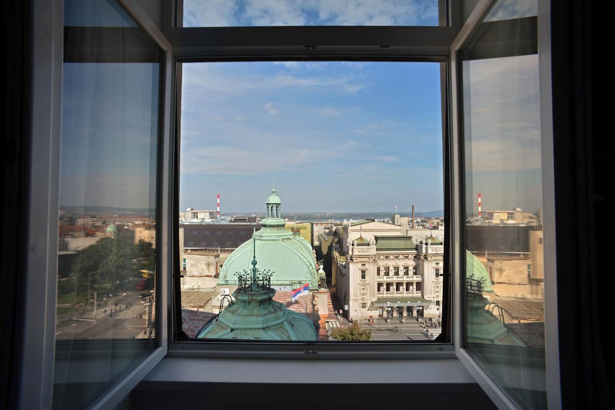 A view through a window of a cityscape with historical buildings and a prominent green dome structure.