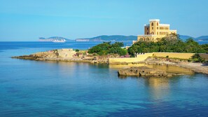 A coastal building with a prominent tower, situated on a rocky shoreline with clear blue waters. - Stylish Studio Just Steps From the sea (Alghero)