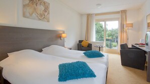Habitación de hotel con dos camas, un escritorio con ordenador, una silla y un balcón con cortinas.