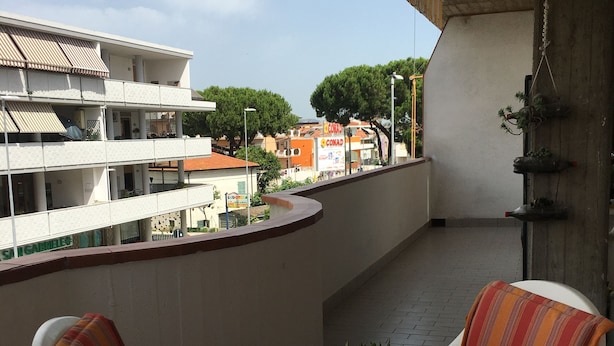En balkon med et bord, stole, en potteplante og udsigt til bygninger og træer.