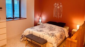 A bedroom with a bed, bench, bedside table, lamp, and a wall hanging. - House 4/5 persons near Puy du Fou (Nueil-les-Aubiers)