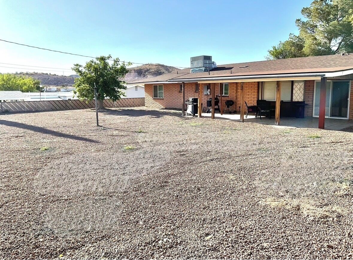 A single-story house with a covered patio, a small tree, and a gravel yard.