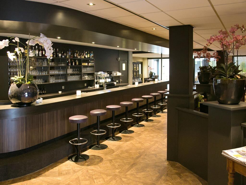 Una zona de bar con una barra larga, varios taburetes y estantes con botellas y vasos.