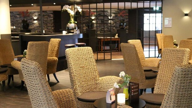 Een hotel lobby met rieten stoelen en tafels, een receptiebalie en een stenen muur.