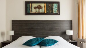 Een netjes opgemaakt bed met twee smaragdgroene kussens, een hoofdbord van donker hout en een kunstwerk erboven.