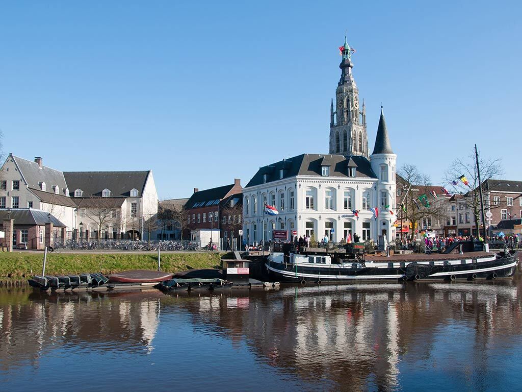 Un bâtiment historique doté d’une tour imposante, un canal où naviguent des bateaux et un ciel d’un bleu éclatant.