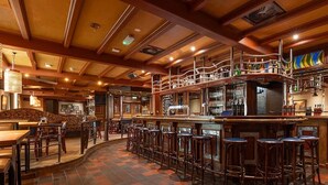 A bar area with wooden bar stools, a counter with bottles, and a tiled floor.