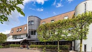 A modern building with a restaurant named 'HENNEBURS' on the ground floor, featuring a brick facade and a curved glass structure.