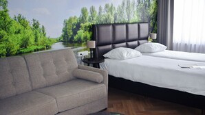 A hotel room with a bed, a sofa, and a view of a river and trees through the window.