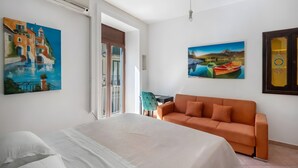 A hotel room with a bed, an orange sofa, and two paintings on the walls. - Francy's Apartment with Balcony, Wi-Fi and Air Conditioning (Salerno)