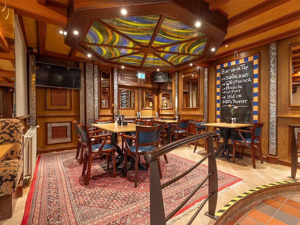 Un restaurante con mobiliario de madera, alfombra estampada y un menú en pizarra.