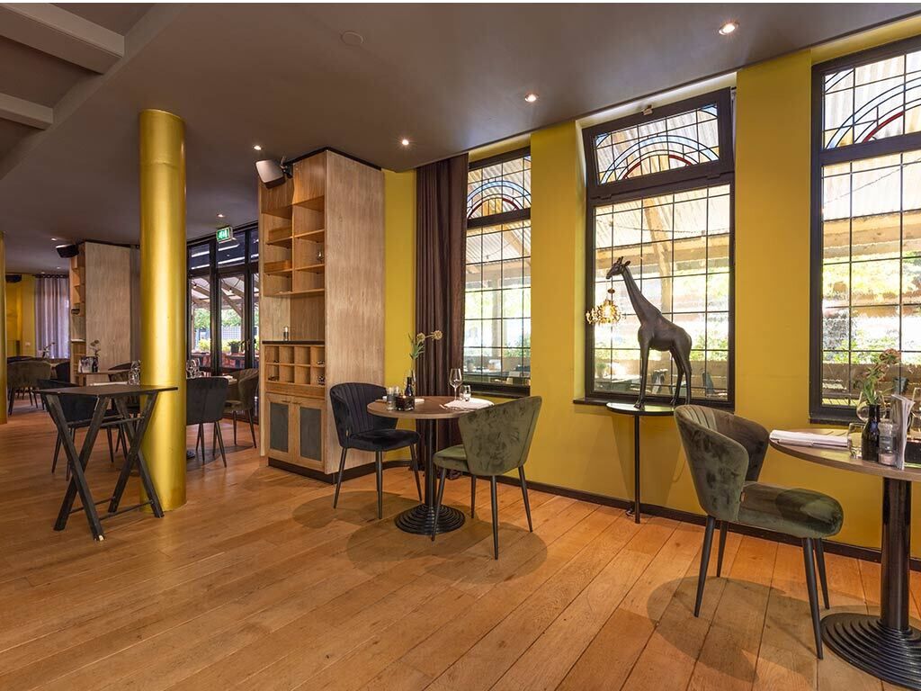 Interior de restaurante com piso de madeira, paredes amarelas e janelas grandes com decoração de girafa.