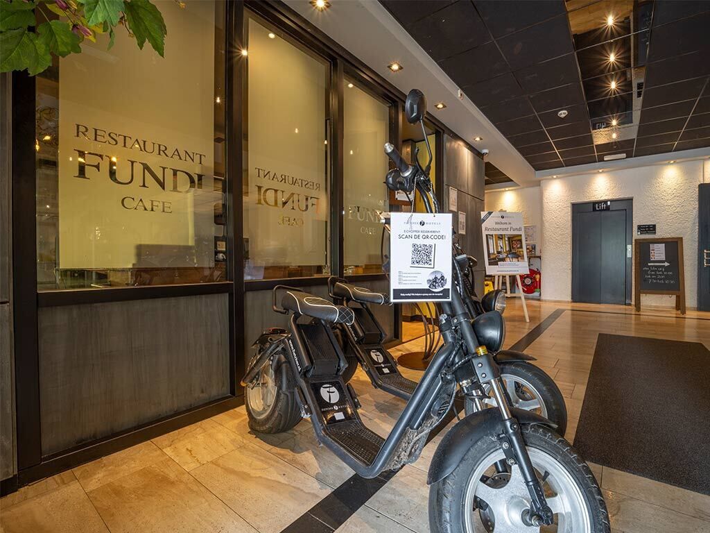 Un restaurant au décor moderne, comprenant un espace salon avec des trottinettes électriques et un panneau avec un code QR.