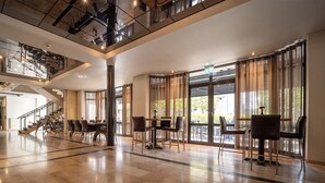 A spacious lobby with a high ceiling, large windows, and a staircase leading to an upper level.