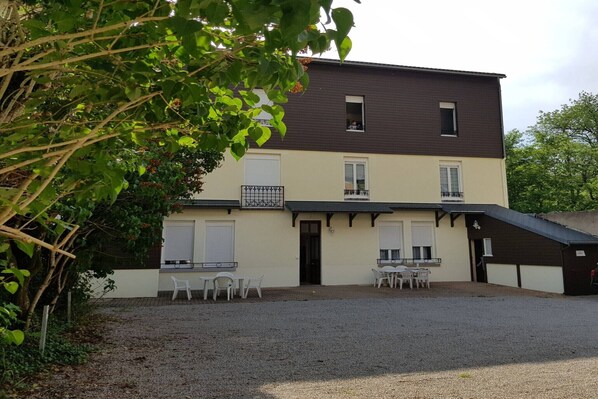 A two-story building with a gravel driveway, a small outdoor seating area with white plastic chairs, and a covered entrance. - Waterfall View Stay for Family (Mont-Dore)
