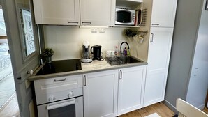 Cocina compacta con armarios blancos, microondas, cafetera y lavamanos.