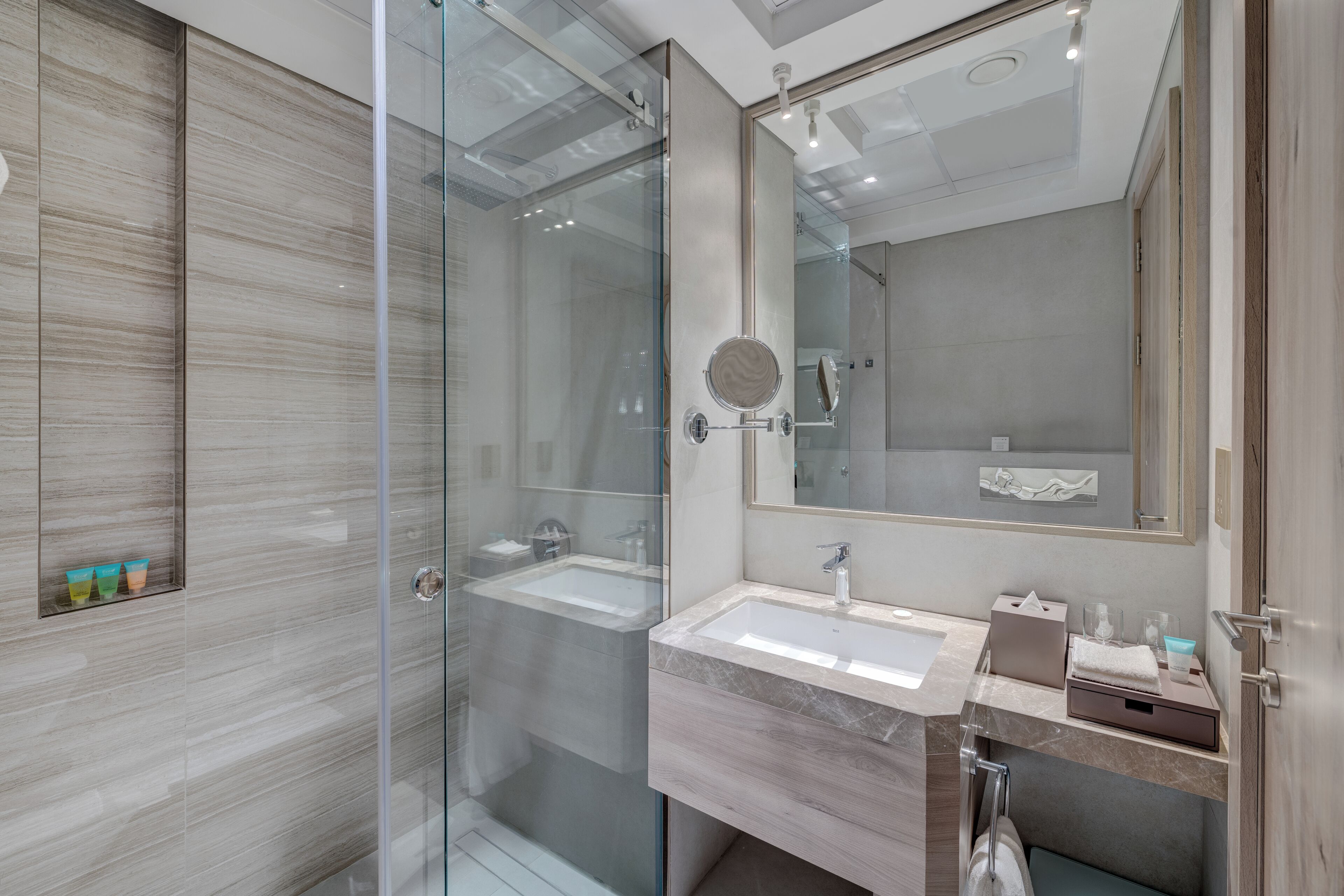A modern bathroom with a glass shower enclosure, a sink with a marble countertop, and a large mirror.