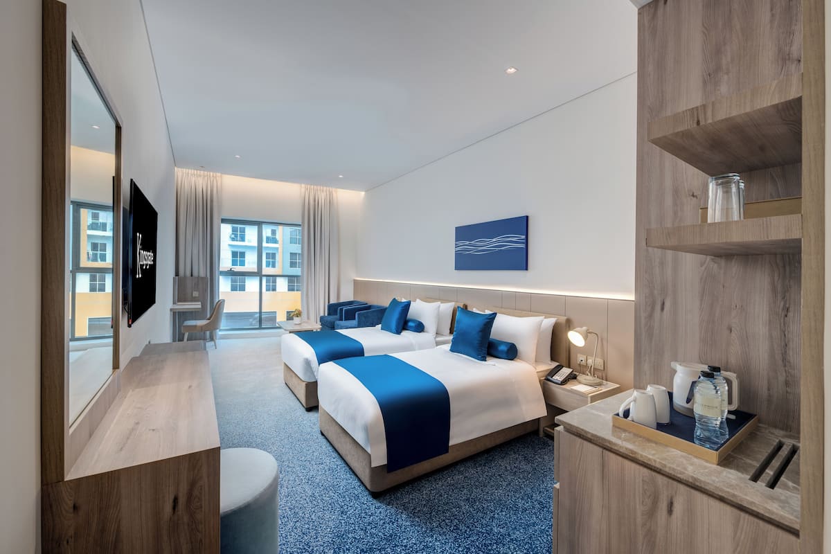 Ein Hotelzimmer mit zwei Betten, einem Schreibtisch, einem Fernseher, einer Kaffeemaschine und Blick auf Gebäude.