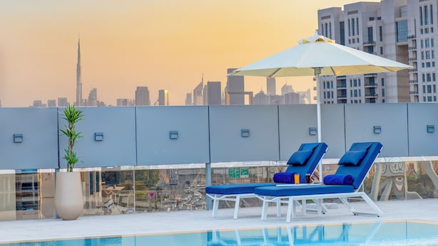 A rooftop pool with two lounge chairs and an umbrella, overlooking a cityscape with high-rise buildings. - Kingsgate Hotel Clocktower (Dubai)