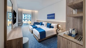 A hotel room with two beds, a desk, a TV, a coffee maker, and a view of buildings. - Kingsgate Hotel Clocktower (Dubai)