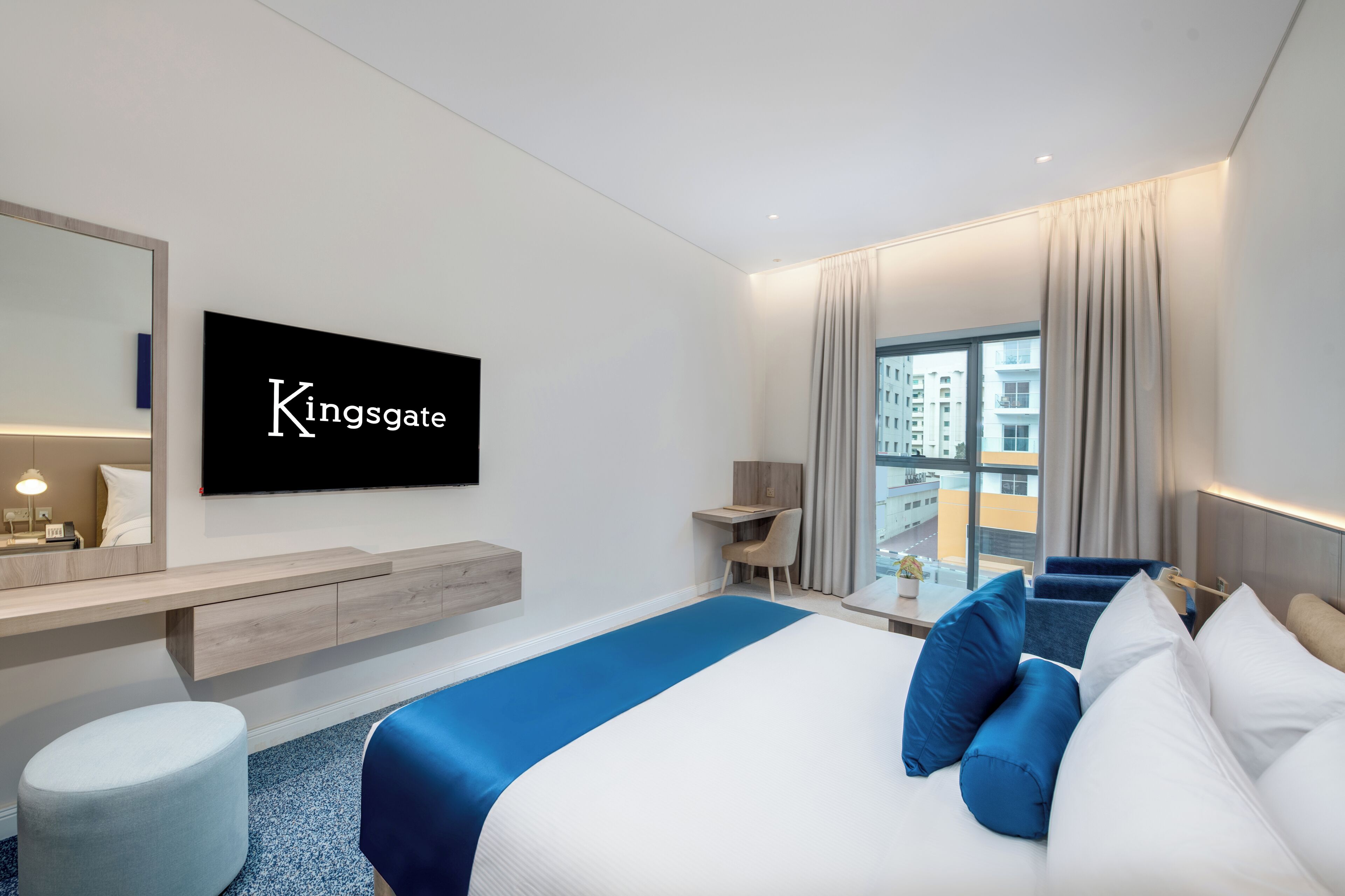 Et moderne hotelværelse med seng, skrivebord, stol, fjernsyn og udsigt over byen.