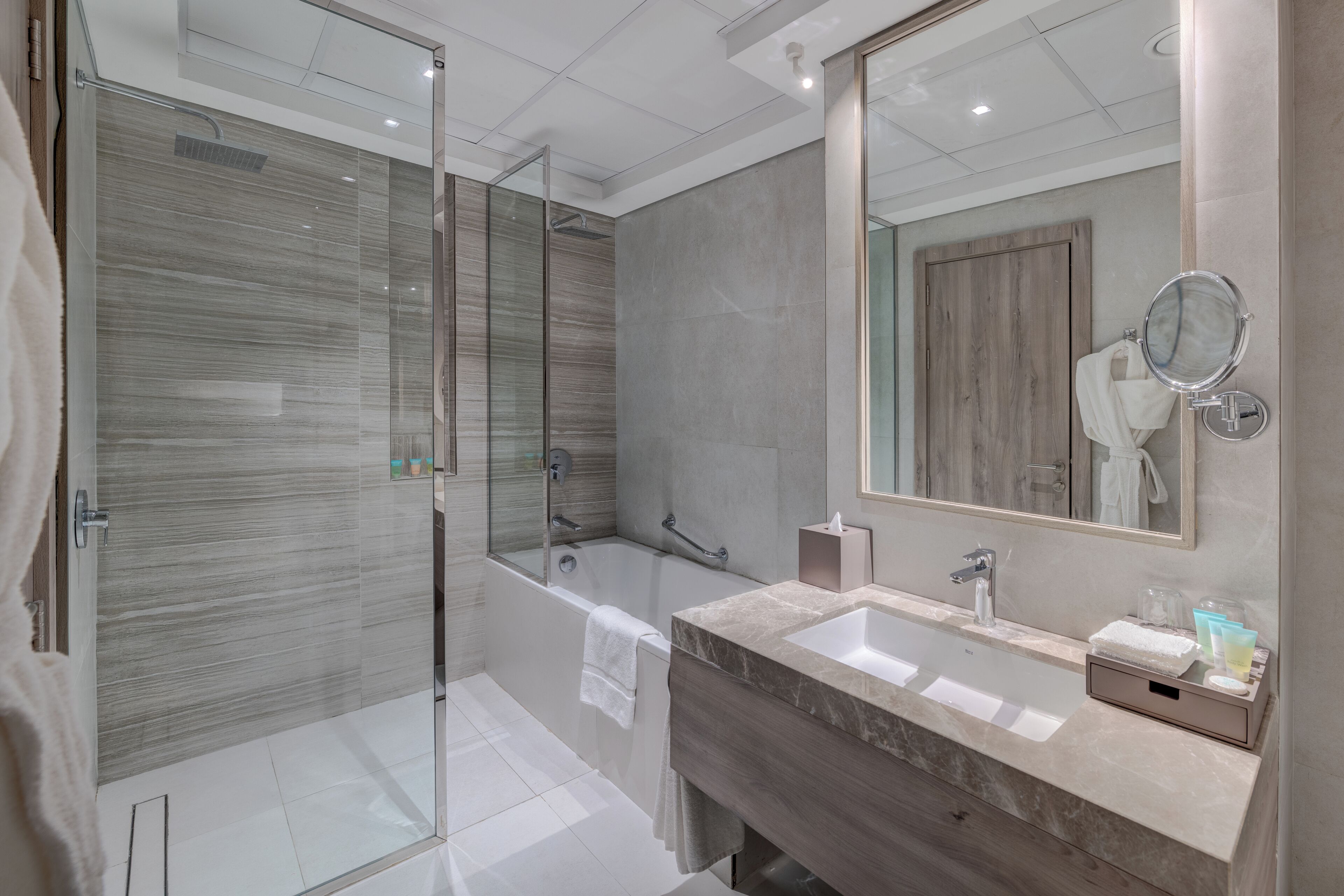Un baño moderno con ducha envuelta en vidrio, una bañera, tocador con lavabo y un espejo grande.