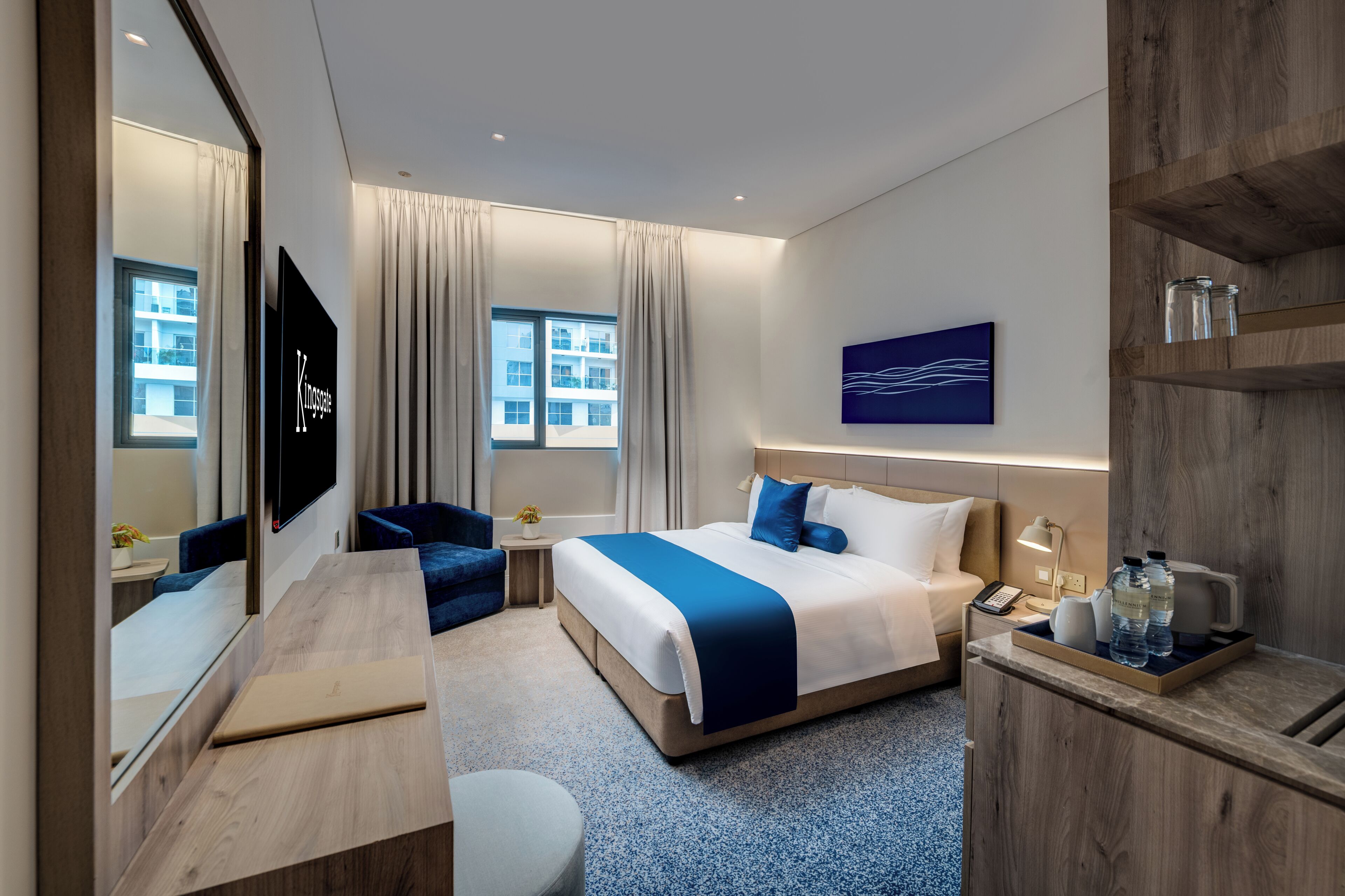 A modern hotel room with a large bed, a desk, a chair, a TV, and a window with curtains.