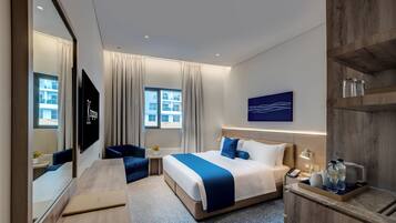 A modern hotel room with a large bed, a desk, a chair, a TV, and a window with curtains.