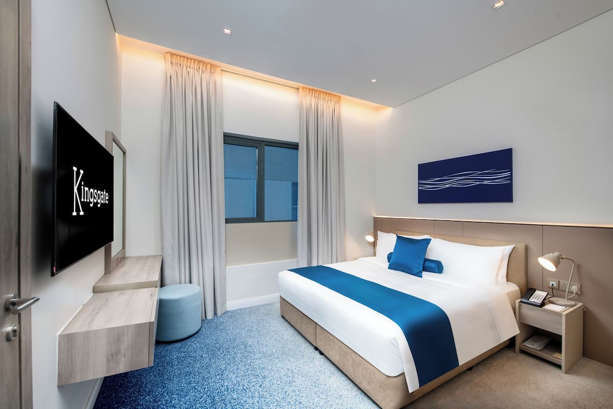 Ein modernes Hotelzimmer mit Bett, Fernseher, Nachttisch und einem Fenster mit Vorhängen.