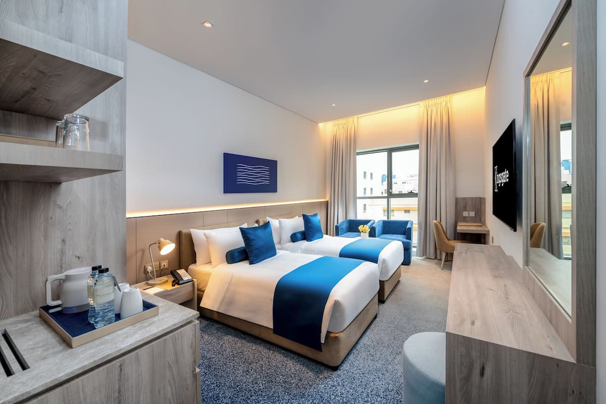 Ein modernes Hotelzimmer mit zwei Betten, einem Schreibtisch, einem Fernseher und einem großen Fenster.