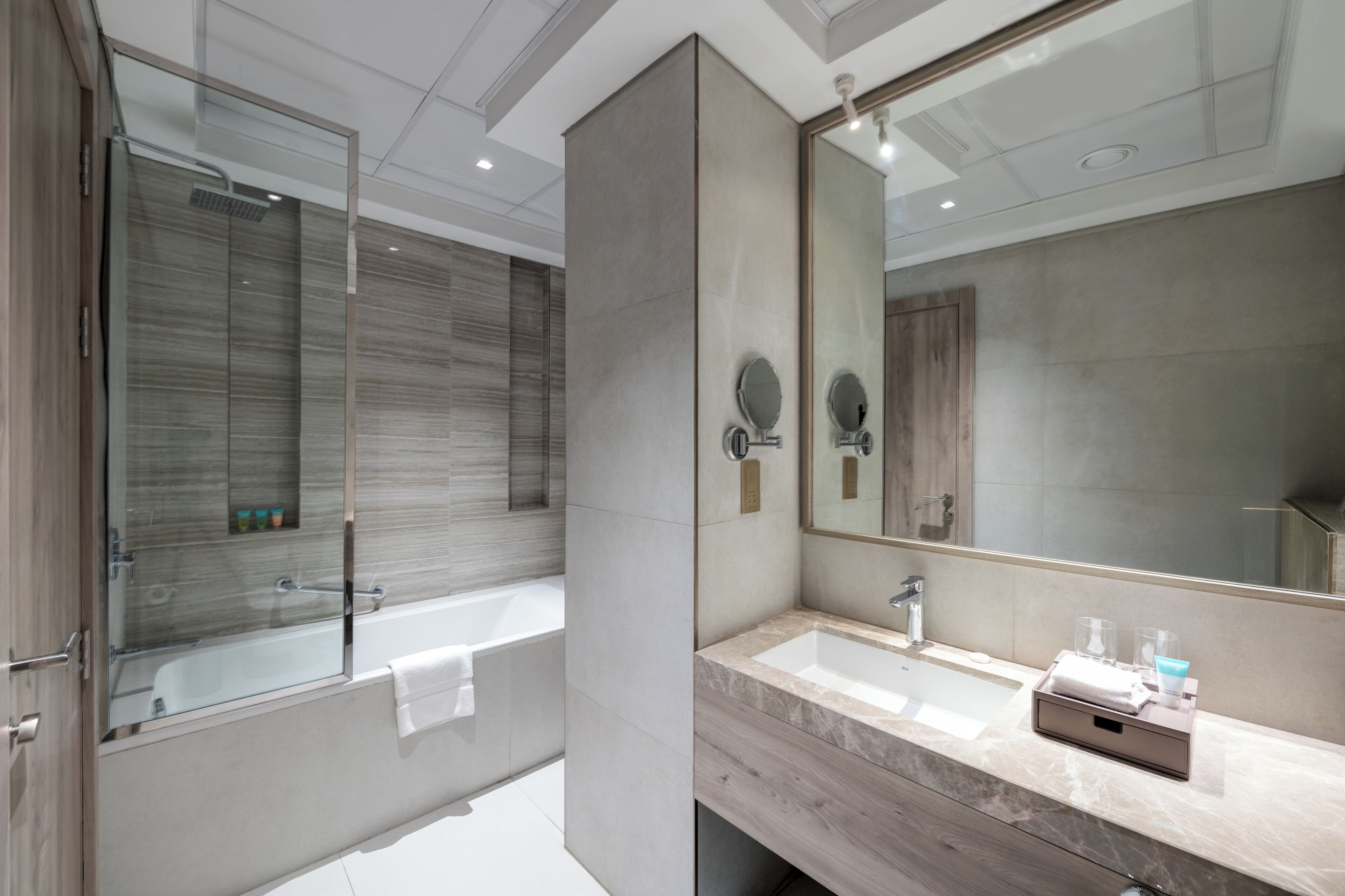 A modern bathroom with a glass-enclosed shower, a large mirror, and a marble countertop.