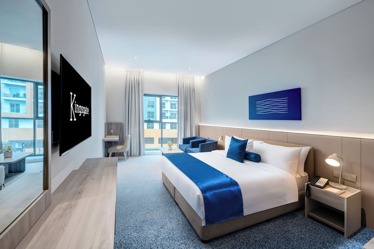 Ein modernes Hotelzimmer mit einem großen Bett, einem Schreibtisch, einem Stuhl, einem Fernseher und einem Fenster mit Blick auf die Stadt.