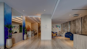 A modern hotel lobby with a reception desk, seating area, and a large mirror reflecting the space. - Kingsgate Hotel Clocktower (Dubai)