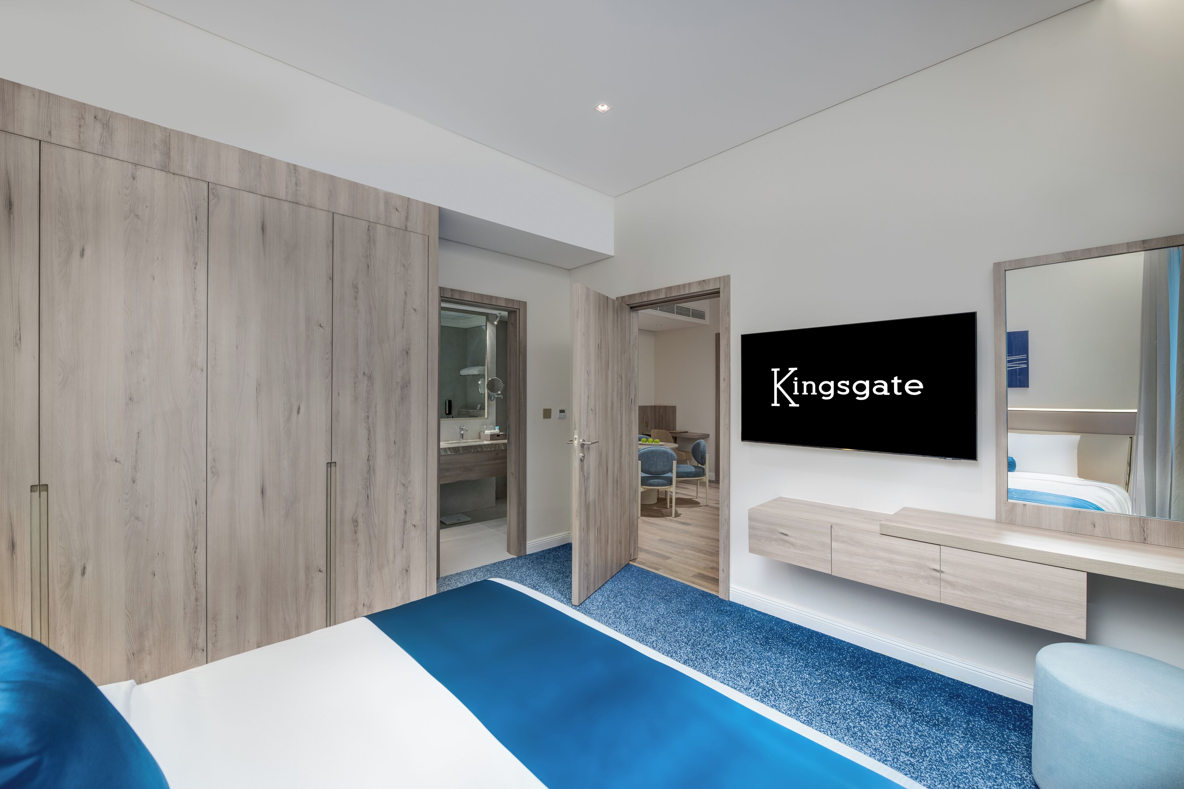 A modern hotel room with a large bed, a TV, a mirror, and a wardrobe.
