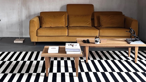 A living room with a mustard sofa, a floor lamp, a wooden coffee table, and a black and white striped rug. - hellofrom Tobacco Warehouse (Kavala)
