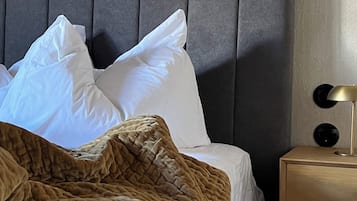 Ein ordentlich bezogenes Bett mit weißen Kissen und einer braunen Decke, ein grauer möbelbezogener Kopfteil und ein Nachttisch mit einer Lampe.