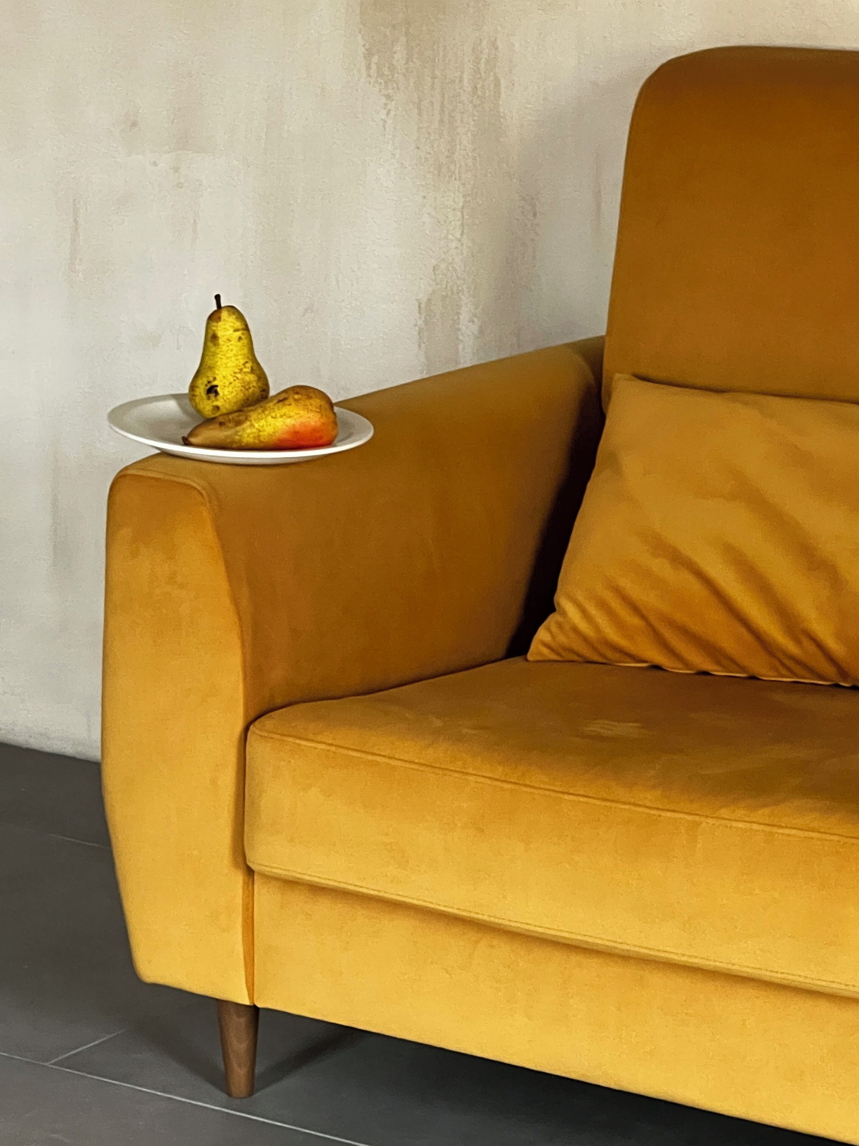 Un sofá color mostaza con un plato de fruta sobre una mesita auxiliar.