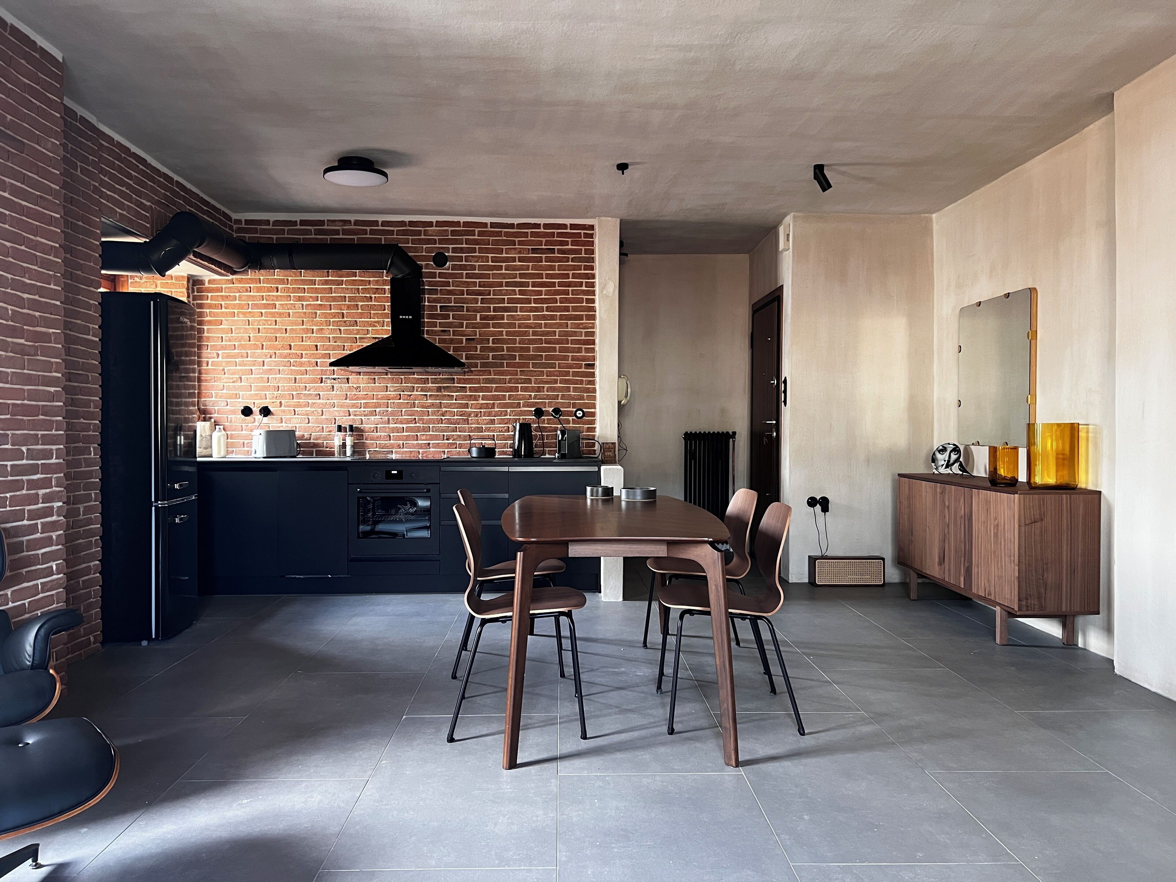 Eine moderne Küche mit Backsteinwand, einer schwarzen Dunstabzugshaube und einem Essbereich mit Holztisch und -stühlen.